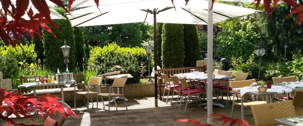 Die grüne Gartenterrasse des Kreuzberg mit gedeckten Tischen und Sonnenschirmen